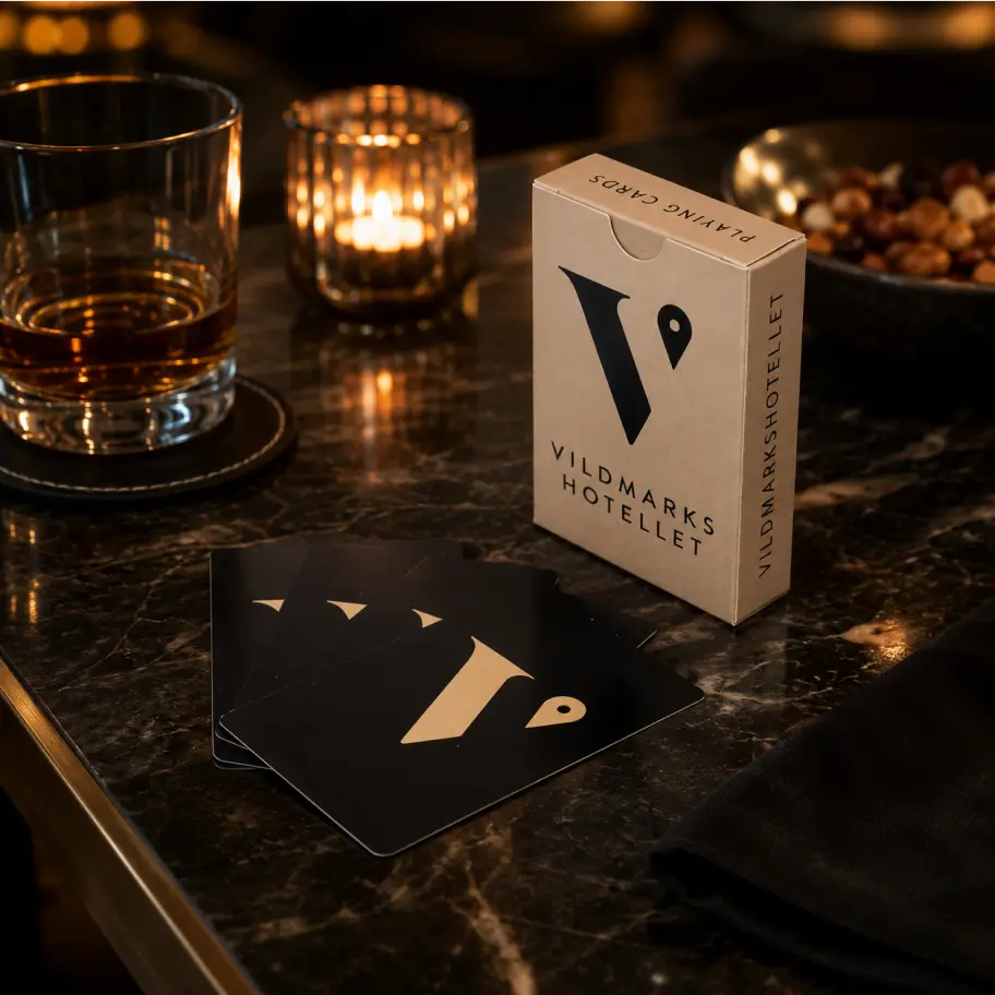 Vildmarkshotellets kortl&aring;da med svarta spelkort, whisky och ljus p&aring; m&ouml;rkt marmorbord.